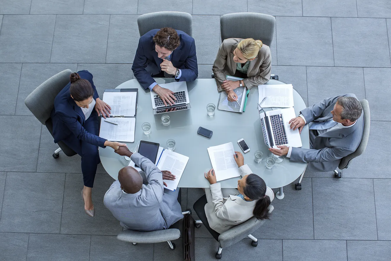 Overhead view of businesspeople shaking hands at conference table in office.