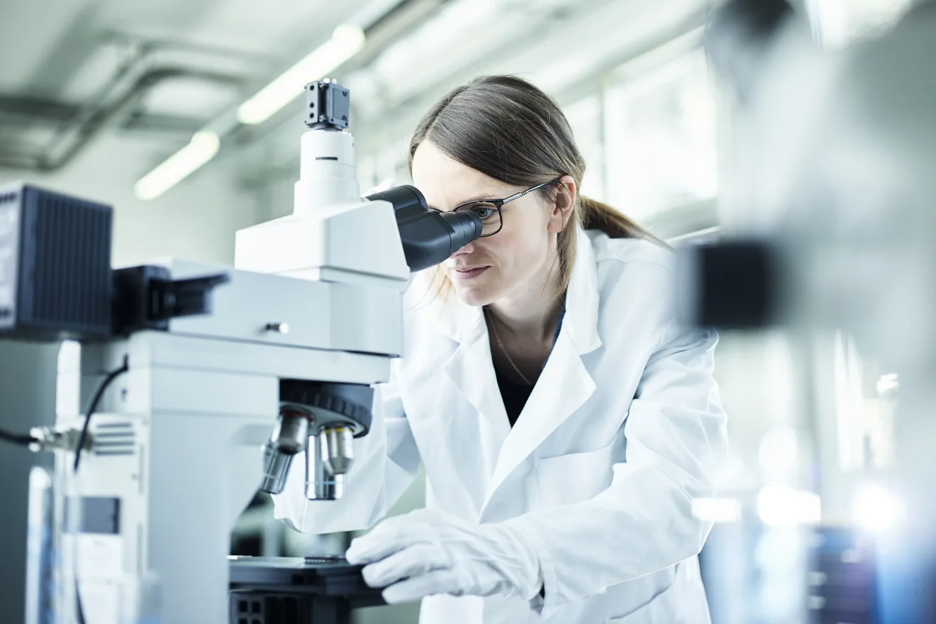 Laboratory technician looking through microscope in lab. Originally used in the Lonza Tampa Visitor Guide.